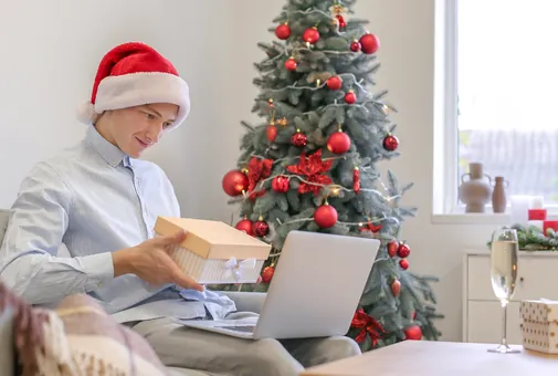Jeune homme ouvrant un cadeau à côté de son sapin de Noël