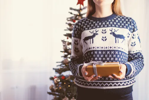 Femme tenant un cadeau devant son sapin de Noël